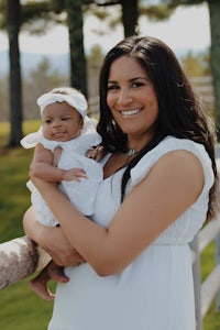 a woman in a white dress holding a baby in front of a fence