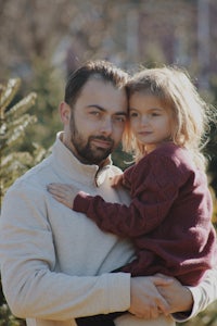 a man holding a little girl in front of a christmas tree farm