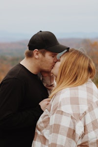 a couple kissing on top of a hill with mountains in the background