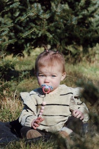 a baby is sitting in the grass with a pacifier in her mouth