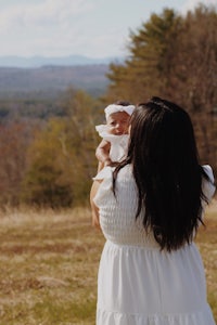 a woman holding a baby in a field with mountains in the background