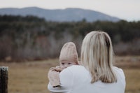 a woman holding a baby in a field with mountains in the background