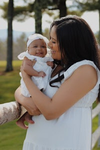 a woman is holding her baby in front of a fence